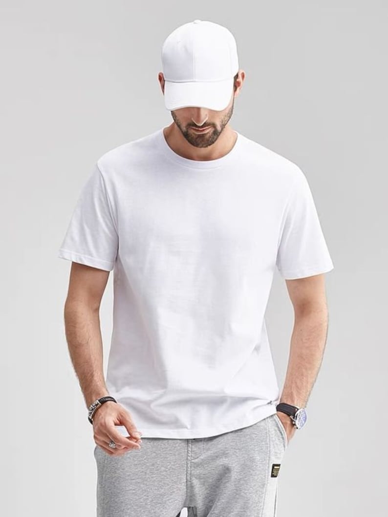 May include: A white short-sleeved t-shirt with a crew neck. The person is wearing a white baseball cap.