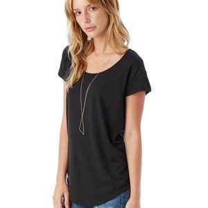 May include: A black short-sleeved t-shirt with a scoop neck and a relaxed fit. The model is wearing the shirt with blue jeans and a gold necklace.