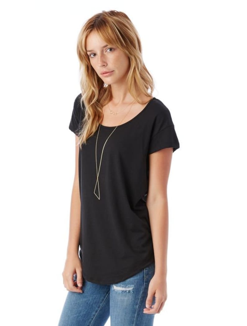 May include: A black short-sleeved t-shirt with a scoop neck and a relaxed fit. The model is wearing the shirt with blue jeans and a gold necklace.