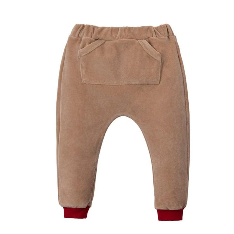 May include: Tan baby pants with a large front pocket and red cuffs. The pants have a relaxed fit and an elastic waistband. The fabric appears soft and plush.