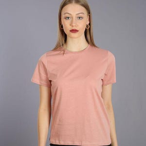 May include: A woman is wearing a light pink short-sleeved t-shirt with a crew neck and black leggings.