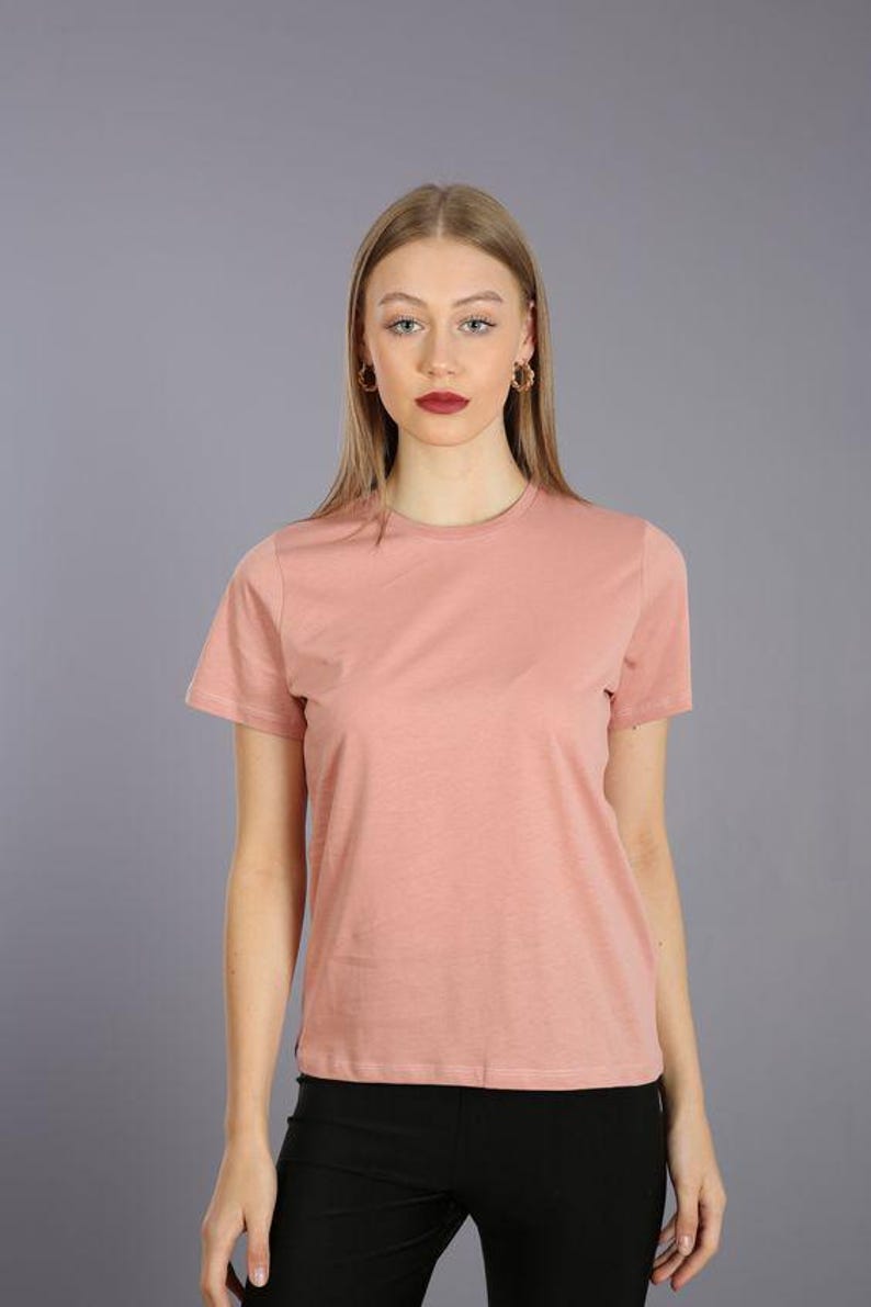 May include: A woman is wearing a light pink short-sleeved t-shirt with a crew neck and black leggings.