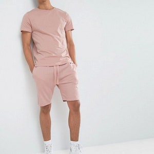 Puede incluir: Un conjunto de camiseta y pantalones cortos de color rosa. La camiseta tiene cuello redondo y los pantalones cortos tienen cintura con cord&oacute;n.