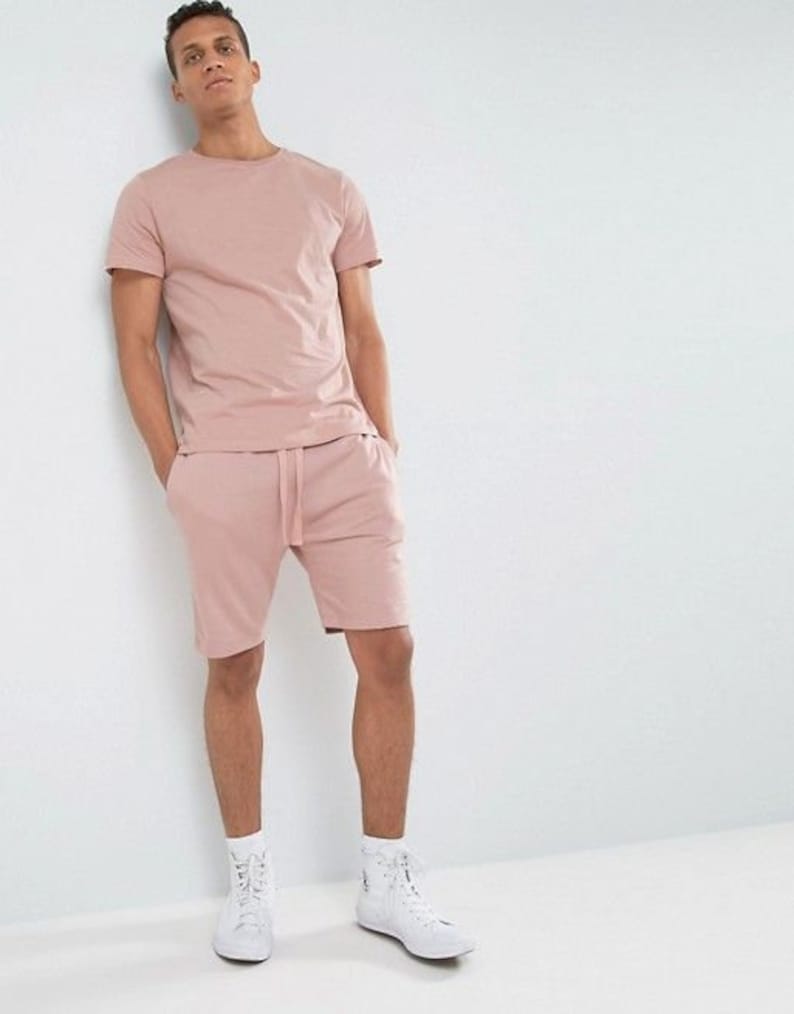 Puede incluir: Un conjunto de camiseta y pantalones cortos de color rosa. La camiseta tiene cuello redondo y los pantalones cortos tienen cintura con cord&oacute;n.