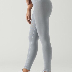 May include: A pair of gray leggings with a high waist and a subtle textured pattern. The leggings are worn by a person with white sneakers.