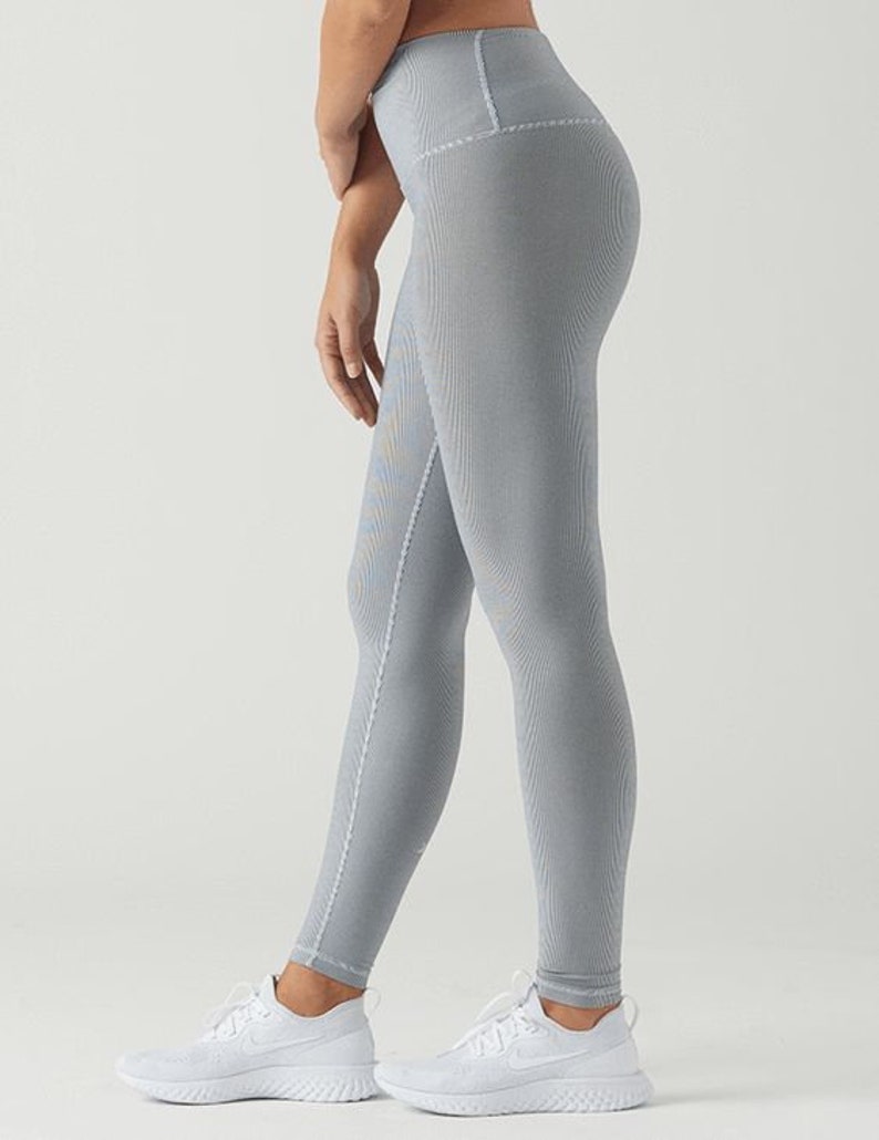 May include: A pair of gray leggings with a high waist and a subtle textured pattern. The leggings are worn by a person with white sneakers.