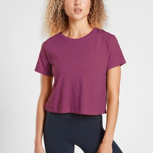 K&ouml;nnte beinhalten: Ein kurz&auml;rmeliges, bauchfreies T-Shirt in einem tiefen Magenta-Farbton. Das Shirt hat einen Rundhalsausschnitt und eine l&auml;ssige Passform. Kombiniert mit dunkelblauen Leggings ist dieses Outfit f&uuml;r sportliche Aktivit&auml;ten oder den Alltag geeignet.