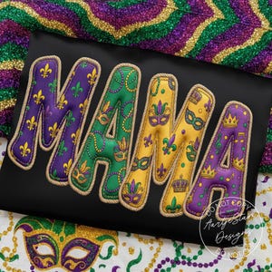 May include: Black fabric with the word "MAMA" in large, padded letters. Each letter is a different color: purple, green, yellow, and purple again. The letters are decorated with Mardi Gras symbols and outlined with a rope-like trim.