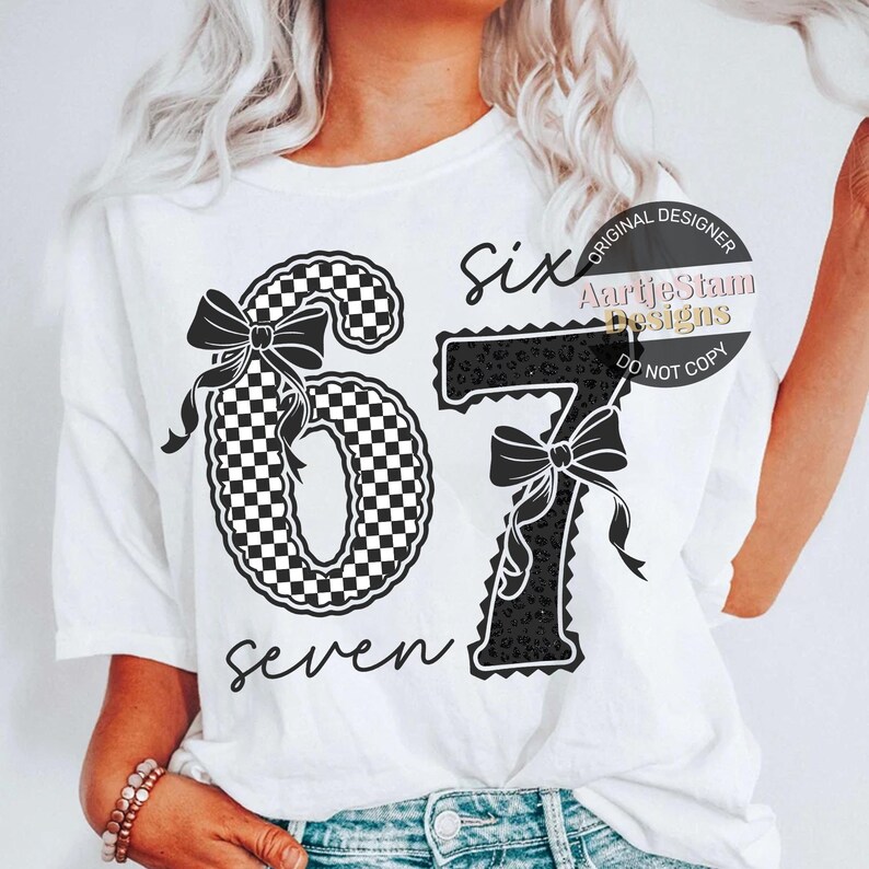 May include: White t-shirt featuring the numbers "67" with decorative bows. The number "6" has a black and white checkered pattern, while the "7" has a black leopard print. The word "six" and "seven" are written in script.
