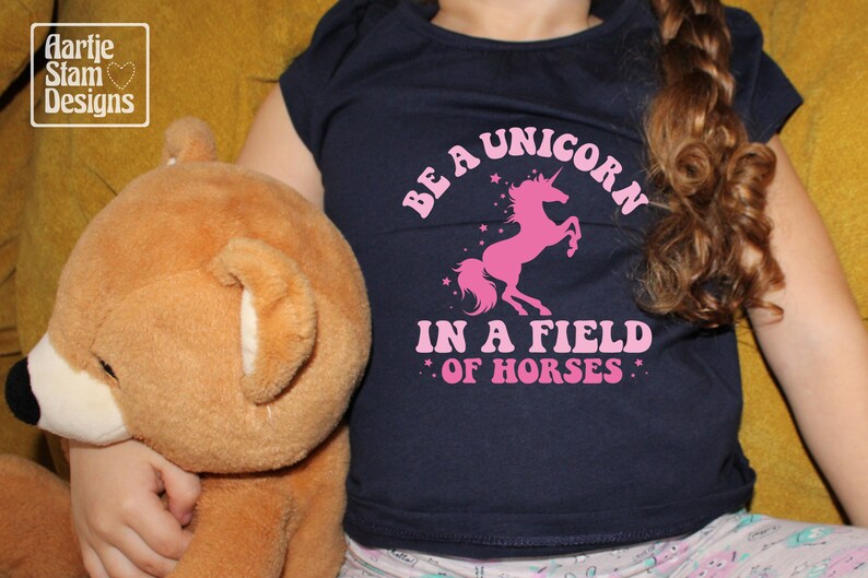 May include: A navy blue t-shirt with a pink unicorn graphic and the text "Be a unicorn in a field of horses".
