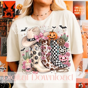 Könnte beinhalten: Ein cremefarbenes T-Shirt mit einem Grafikdruck, der einen Cowboyhut mit rosa Schleife, drei Cowboystiefel mit Blumen-, Kuhfell- und Schachbrettmuster, Kürbisse, Kakteen, Rosen, Spinnennetze, Fledermäuse und eine brennende Kerze mit Fledermaus-Symbol zeigt.
