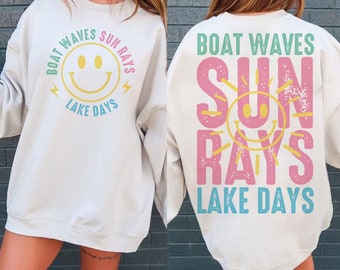 Könnte beinhalten: Cremefarbenes Sweatshirt mit den Aufschriften "Boat Waves Sun Rays Lake Days" und einem gelben Smiley-Gesicht. Auf der Rückseite des Sweatshirts wiederholen sich die Sätze und das Smiley-Gesicht in vertikaler Anordnung.