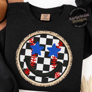 Könnte beinhalten: Schwarzes Sweatshirt mit einem Smiley-Gesicht-Design. Das Smiley-Gesicht hat einen karierten Hintergrund, blaue Sternaugen und rote Baseballnähte. Das Design ist mit einem beigefarbenen, strukturierten Rand umrandet. Der Text "Original Designer AartjeStam Designs DO NOT COPY" befindet sich oben rechts.