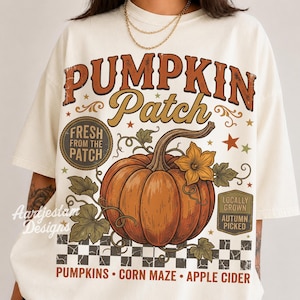 Könnte beinhalten: Ein cremefarbenes T-Shirt mit einer großen Grafik eines orangefarbenen Kürbisses mit grünen Blättern und einer gelben Blüte. Der Text lautet PUMPKIN Patch, FRESH FROM THE PATCH, LOCALLY GROWN, AUTUMN PICKED, PUMPKINS, CORN MAZE und APPLE CIDER.