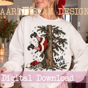 Könnte beinhalten: Ein weißes Langarm-Sweatshirt mit einer Grafik, die den Weihnachtsmann kopfüber in einem Tannenbaum steckend zeigt. Das Motiv umfasst rot-weiß gestreifte Beine, schwarze Stiefel, eine karierte Mütze, Tannenzapfen und den Text Well, shit...