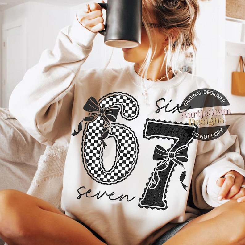 May include: Cream-colored sweatshirt featuring a black and white checkered number six with a bow, and a black number seven with a bow and leopard print. The word "seven" is written below the number six.