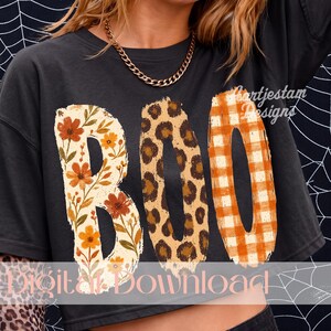 Könnte beinhalten: Ein schwarzes T-Shirt mit dem Wort BOO in großen Buchstaben. Das B hat ein Blumenmuster mit orangefarbenen und gelben Blüten, das O ein braun-beiges Leopardenmuster und das zweite O ein orange-weißes Vichy-Karo-Muster.