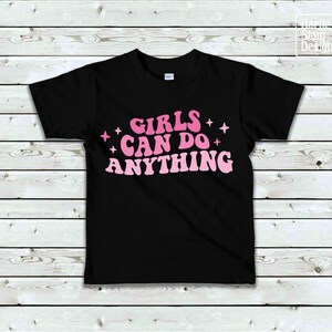 May include: Black t-shirt with pink text that reads "Girls Can Do Anything" with pink stars on either side of the text.