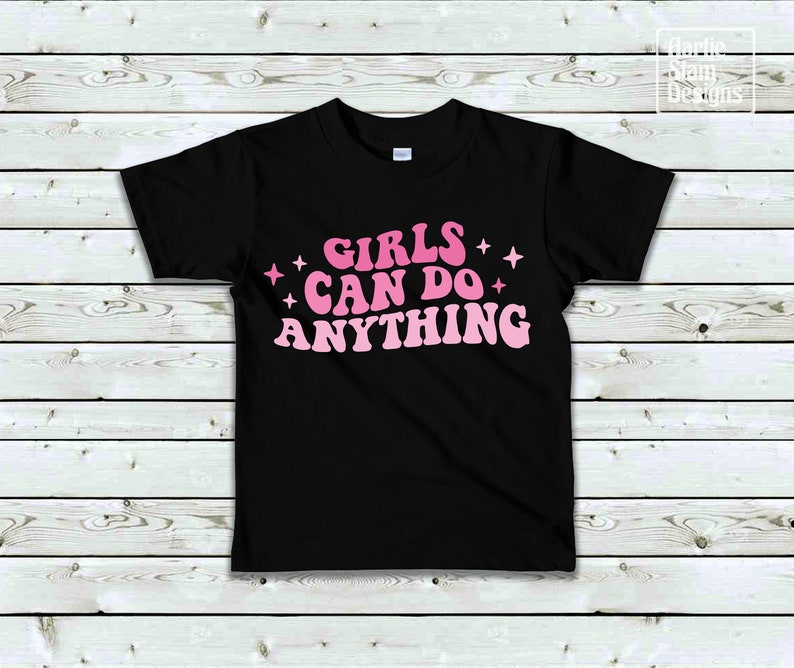 May include: Black t-shirt with pink text that reads "Girls Can Do Anything" with pink stars on either side of the text.