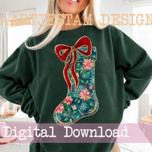 May include: A dark green long-sleeve sweatshirt featuring a central graphic of a Christmas stocking. The stocking is decorated with red poinsettias, white snowflakes, candy canes, and small gift boxes, topped with a large red bow with gold trim.