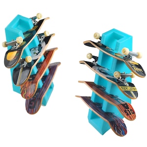 May include: A turquoise plastic stand with five fingerboard skateboards stacked on top of each other. The skateboards have various designs and graphics, including "Reime" and "NYJAH".