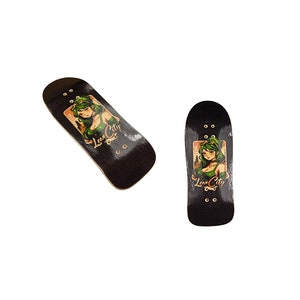 Puede incluir: Dos fingerboards negros con un gr&aacute;fico de una mujer con cabello verde y el texto "Lean City".