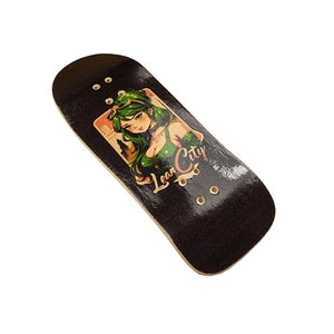 Puede incluir: Un fingerboard negro con un gr&aacute;fico de una mujer con cabello verde y el texto "Lean City".