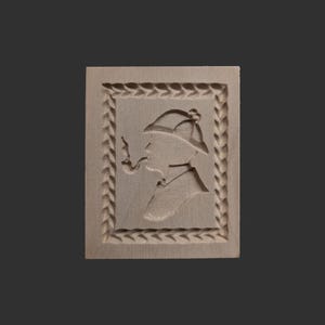 Könnte beinhalten: Ein Holz-Ausstecher in Form einer Person mit Hut und Pfeife. Der Ausstecher hat einen dekorativen Rand.