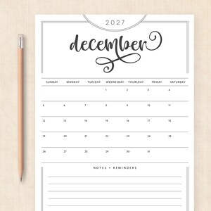 May include: A white calendar page for December 2027 with black text and lines, featuring a decorative script font for the month name, a grid for the days of the week, and a section for notes and reminders, accompanied by a wooden pencil.