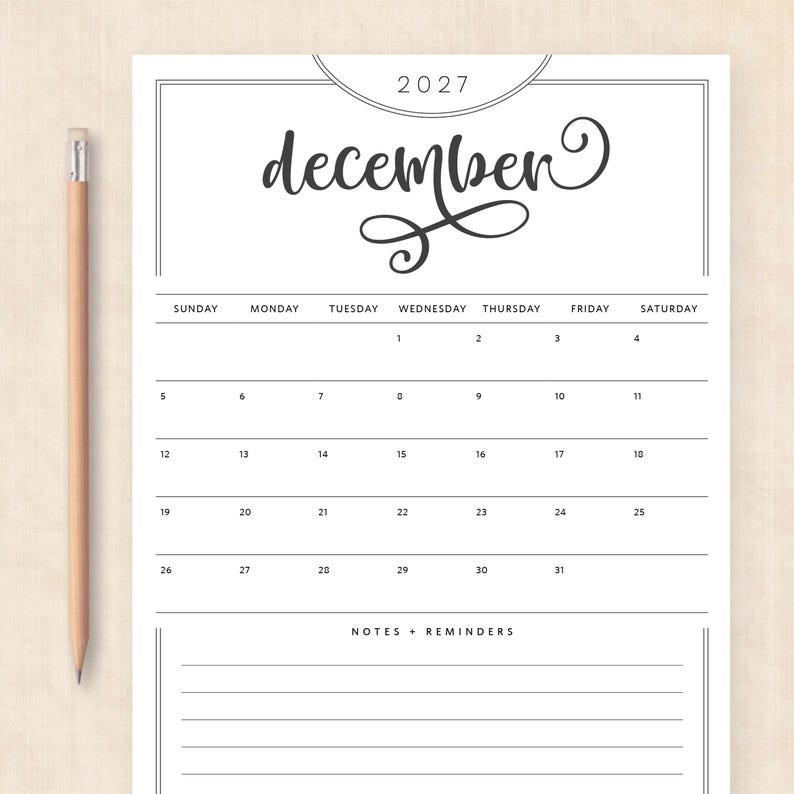 May include: A white calendar page for December 2027 with black text and lines, featuring a decorative script font for the month name, a grid for the days of the week, and a section for notes and reminders, accompanied by a wooden pencil.