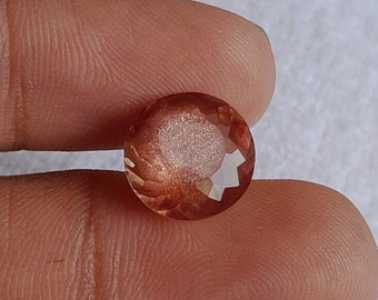 May include: A round, faceted, orange sunstone gemstone with a shimmery, iridescent finish.