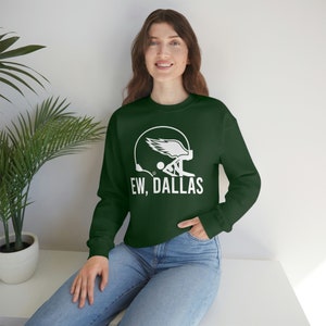 May include: A dark green sweatshirt with a white graphic of a football helmet with wings and the text "EW, DALLAS".