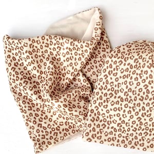 May include: A beige beanie and matching neck warmer with a brown leopard print pattern.