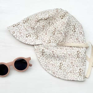 Könnte beinhalten: Ein beiger Sonnenhut mit Leopardenmuster und eine passende runde, rosa Sonnenbrille. Der Hut hat eine breite Krempe und einen Kordelverschluss. Die Sonnenbrille hat schwarze Gläser.