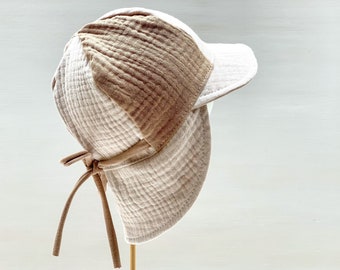 May include: A beige and white sun hat with a wide brim and a tie at the back. The hat is made of a soft, textured fabric.