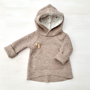 May include: A brown hooded sweatshirt with a white lining featuring a moon and star pattern. The sweatshirt has a kangaroo pocket and long sleeves with cuffed ends.