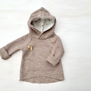May include: A brown hooded sweatshirt with a white lining featuring a small moon and star pattern. The sweatshirt has a kangaroo pocket and long sleeves.