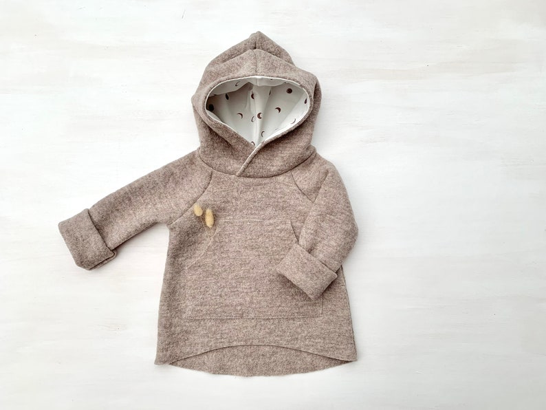 May include: A brown hooded sweatshirt with a white lining featuring a small moon and star pattern. The sweatshirt has a kangaroo pocket and long sleeves.