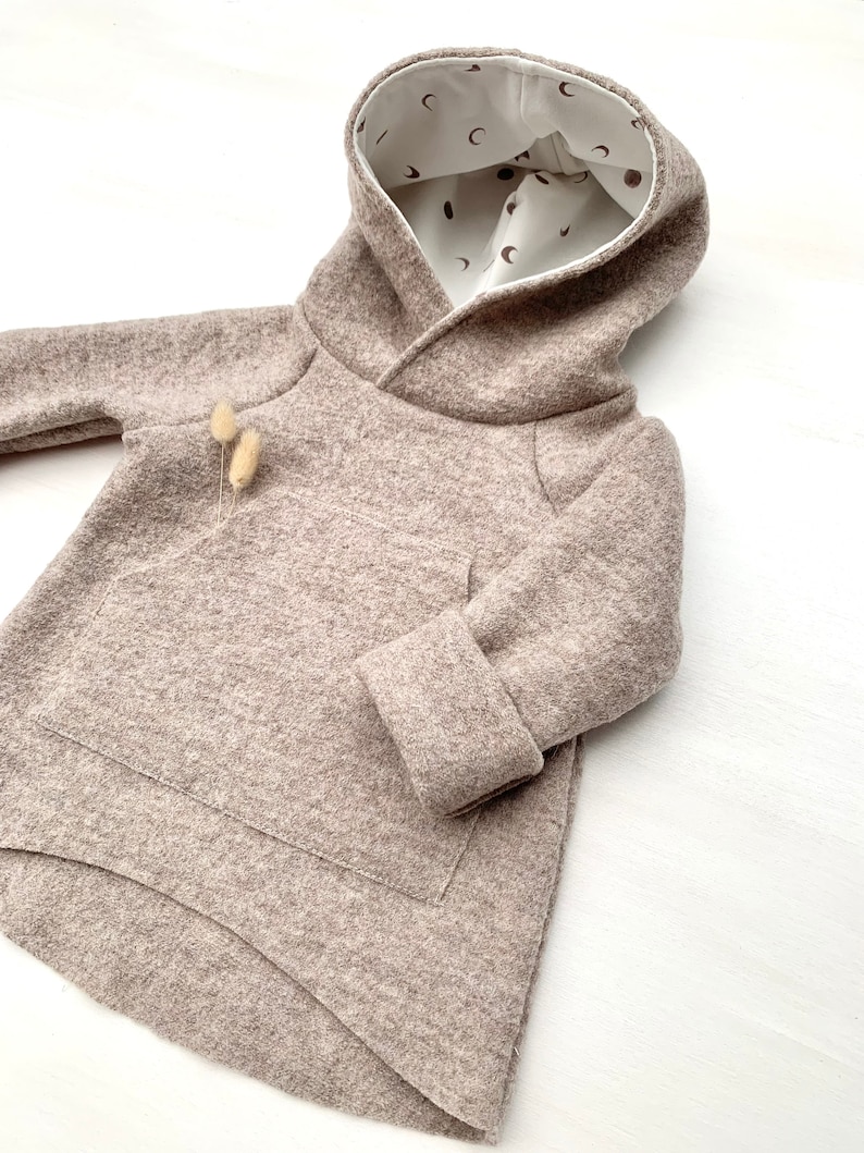 May include: A brown hooded sweatshirt with a white lining featuring a pattern of small moons and dots. The sweatshirt has a kangaroo pocket and a curved hem.