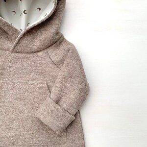 May include: A brown hooded sweatshirt with a white lining featuring a pattern of small brown crescent moons. The sweatshirt has a kangaroo pocket and long sleeves.