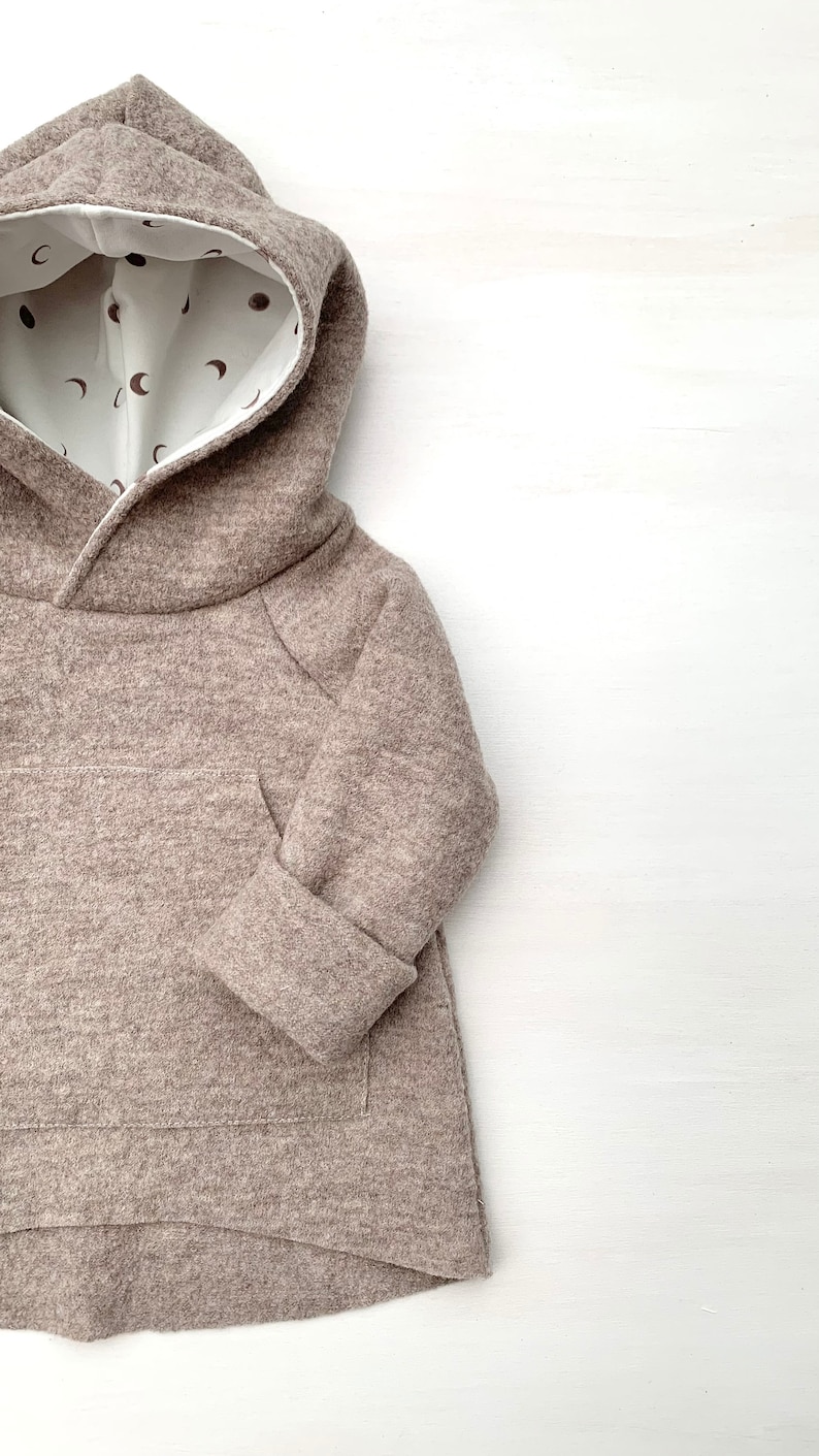 May include: A brown hooded sweatshirt with a white lining featuring a pattern of small brown crescent moons. The sweatshirt has a kangaroo pocket and long sleeves.