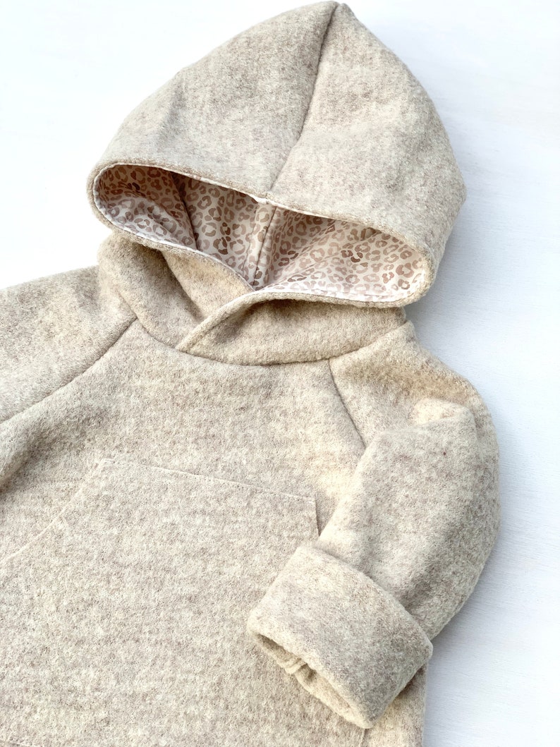 May include: A beige hooded sweatshirt with a brown leopard print lining. The sweatshirt has a pocket on the front and long sleeves with cuffed ends.