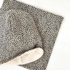 May include: A beige and black leopard print fabric headband with a cream-colored lining. The headband is folded in half and the lining is visible.
