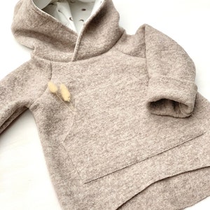 May include: A brown hooded sweatshirt with a pocket on the front. The hood is lined with a white fabric with a brown crescent moon pattern.