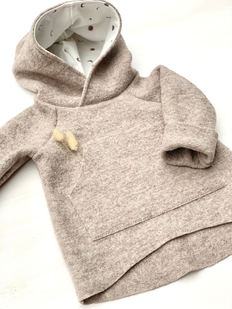 May include: A brown hooded sweatshirt with a pocket on the front. The hood is lined with a white fabric with a brown crescent moon pattern.