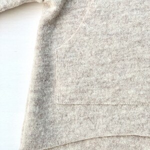 May include: A close-up of a light brown, fuzzy sweater with a large pocket on the front. The sweater is made of a soft, comfortable material.