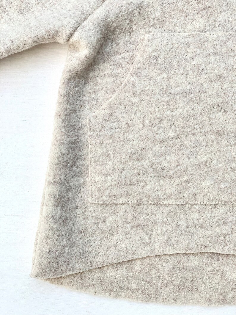May include: A close-up of a light brown, fuzzy sweater with a large pocket on the front. The sweater is made of a soft, comfortable material.