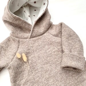 May include: A brown hooded sweatshirt with a white lining featuring a pattern of small brown moons. The sweatshirt has a kangaroo pocket and a contrasting brown trim around the hood.