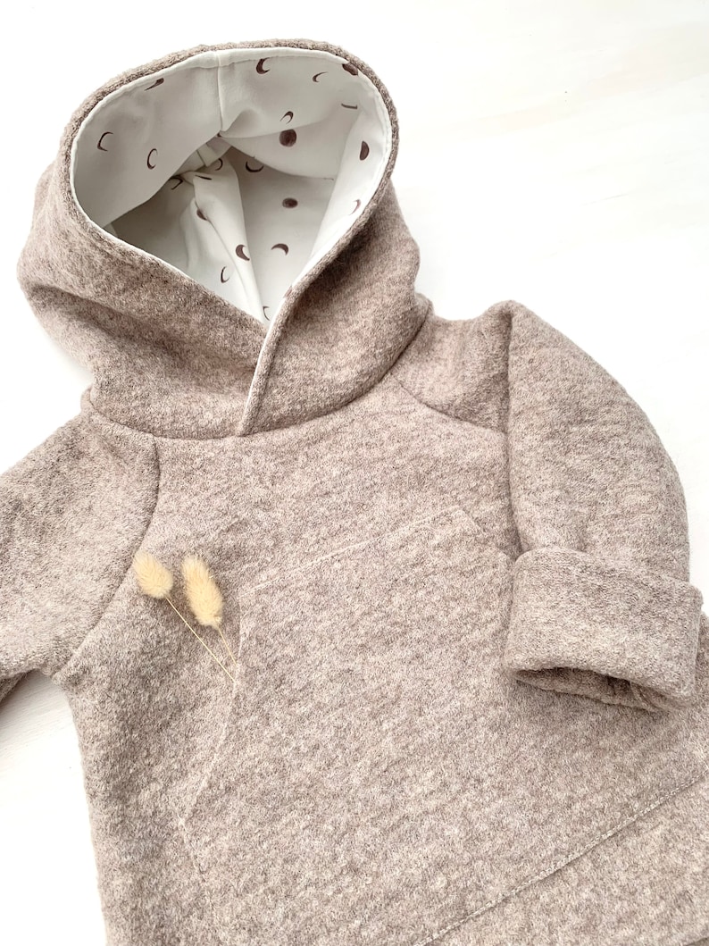 May include: A brown hooded sweatshirt with a white lining featuring a pattern of small brown moons. The sweatshirt has a kangaroo pocket and a contrasting brown trim around the hood.