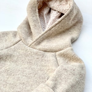May include: A beige hooded sweatshirt with a leopard print lining. The sweatshirt is made of a soft, fuzzy fabric.